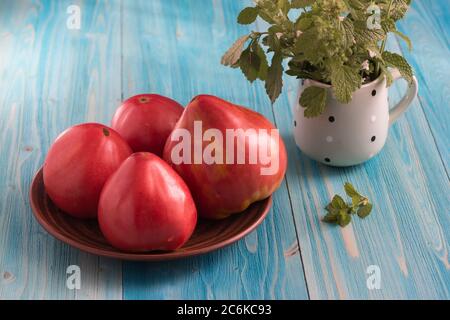 Pomodori rosa rustici su un tavolo di legno blu. Nella tazza - un mazzo di Melissa Foto Stock