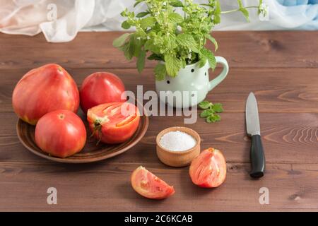 Grandi pomodori rosa di campagna succosi maturi e un salamoia su un tavolo di legno. Nella tazza - un mazzo di Melissa Foto Stock