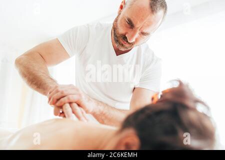 Uomo massaggiatore con braccio che effettua manipolazioni di massaggio sulla zona di Scapula durante il massaggio femminile. Foto Stock