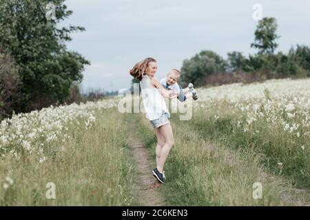 Madre sorridente che gioca con il suo figlio in natura. Mamma che tiene il figlio nelle braccia e fa piano. Madre e figlio. Buona famiglia Foto Stock