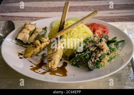 Piatti tipici balinesi con kebab, riso giallo, verdure e pomodori. Bali, Indonesia Foto Stock