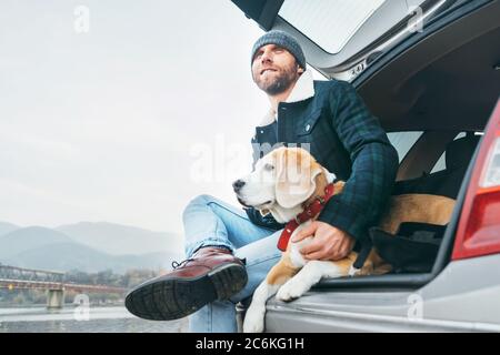 Uomo con cane beagle seduto insieme nel bagagliaio dell'auto Foto Stock