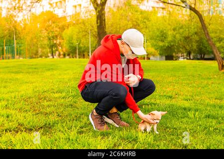 Ritratto di giovane caucasico in felpa rossa, maschera medica di protezione e occhiali da sole rimanere nel parco a giorno di sole. Papà camminare all'aperto con il piccolo carino Foto Stock