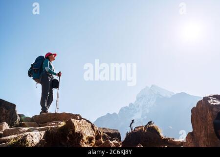 Giovane escursionista zaino in spalla femmina sul bordo della scogliera godendo la montagna Thamserku 6608m durante l'alta altitudine acclimatazione passeggiata. Everest base Camp Trekkin Foto Stock