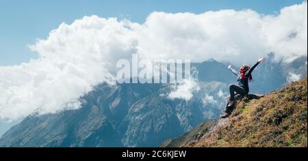 Giovane escursionista zaino in spalla femmina alzando le braccia, allegro ridere e godendo valle durante l'alta altitudine Everest base Camp (EBC) percorso di trekking vicino a N Foto Stock