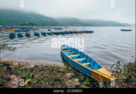 Barche a remi tradizionali multicolore sulle acque del lago mattutino a Pokhara, Gandaki Pradesh, Nepal. Immagine del concetto di viaggio asiatico. Foto Stock