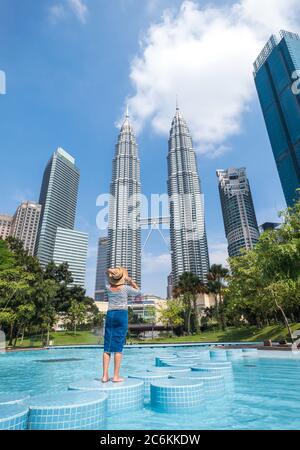 Kuala Lumpur City, Malesia – 12 MARZO 2019: Giovane turista femminile in cappello di paglia che gode di due grattacieli Petronas Towers a Kuala Lumpur Foto Stock