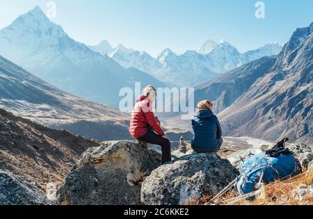 Una coppia simpatica riposante sul percorso di trekking Everest base Camp vicino a Dughla 4620m. Uomo sorridente a woman.Backpackers sinistra zaini e bastoni da trekking e. Foto Stock