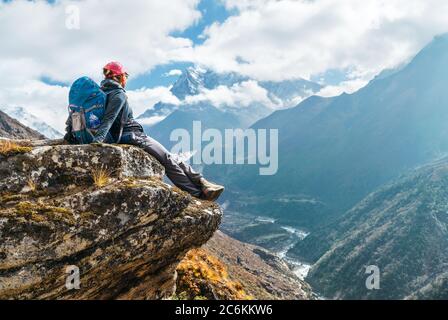 Giovane escursionista zaino in spalla femmina seduto sul bordo della scogliera e godendo di Ama Dablam 6,812 m vista picco durante Everest base Camp (EBC) percorso di trekking vicino pH Foto Stock