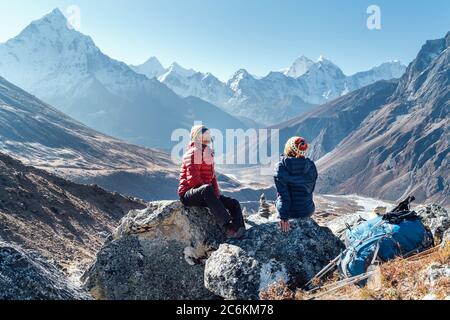 Una coppia simpatica riposante sul percorso di trekking Everest base Camp vicino a Dughla 4620m. Uomo e donna godendo di un Rest.They hanno lasciato zaini e bastoni da trekking An Foto Stock