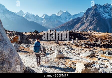 Giovane donna zaino in spalla seguendo il percorso di trekking Everest base Camp utilizzando bastoni da trekking e godendo la vista della valle con la vetta Ama Dablam. È venuta a Eva Foto Stock