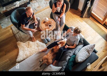 Accogliente tempo di te' per la famiglia. Padre, madre e figlio nel soggiorno di casa. Ragazzo sdraiato in comodo divano e stropicciando il loro cane beagle e sorridendo. Pace Foto Stock