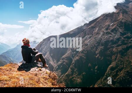 Giovane donna escursionista zaino in spalla seduto sul bordo della cima e godendo di vista montagne valle durante l'alta altitudine Everest base Camp (EBC) percorso di trekking Foto Stock
