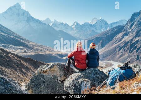 Coppia riposante sul percorso di trekking Everest base Camp vicino Dughla 4620m. Backpackers sinistra zaini e bastoni da trekking e godendo vista valle con Foto Stock