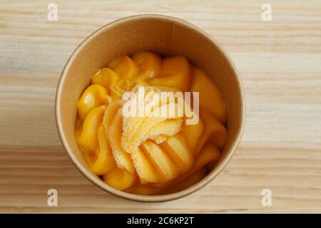 Il sorbetto al mango in una tazza di cartone si trova su un tavolo di legno. Primo piano. Vista dall'alto verso il basso Foto Stock