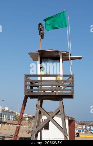 Punta Umbria, Huelva, Spagna - 9 luglio 2020: Un bagnino seduto sulla torre di sorveglianza sulla spiaggia di Punta Umbria, Huelva, Spagna Foto Stock