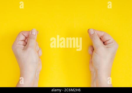 Mani con dita aggrinzite in un pizzico su sfondo giallo Foto Stock