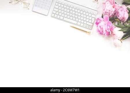 Tastiera, penna dorata, occhiali, calcolatrice e un bouquet di peonie rosa su sfondo bianco. Spazio di copia. Foto Stock