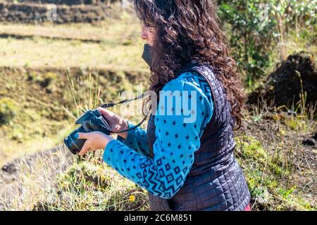 Giovane donna, fotografo professionista, che riesamina e controlla le immagini scattate mentre si siede nell'erba verde Foto Stock