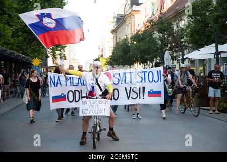 Lubiana, Slovenia. 10 luglio 2020. Un manifestante fa ondate una bandiera slovena che fa girare una bicicletta davanti ai manifestanti che marciano per le strade intorno all'edificio del parlamento durante una protesta anti-governativa.per l'undicesimo venerdì consecutivo, migliaia di persone a Lubiana hanno protestato contro il governo del primo ministro Janez Jansa tra le accuse di corruzione del suo governo, accusare il governo di smantellare la democrazia e di volgersi verso il fascismo. Credit: SOPA Images Limited/Alamy Live News Foto Stock