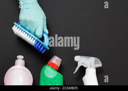 Mano della donna in un guanto protettivo con una spazzola e un set per lavaggio e pulizia su sfondo nero. Vista dall'alto. Foto Stock