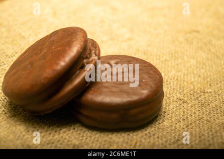 Biscotti ricoperti di cioccolato su uno sfondo di tessuto casalinga con una consistenza ruvida. Primo piano Foto Stock