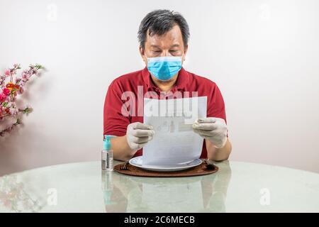 Concettuale dell'uomo asiatico con maschera facciale, guanto e disinfettante che guarda al menu usa e getta al ristorante, come parte del nuovo stile di vita normale. Foto Stock