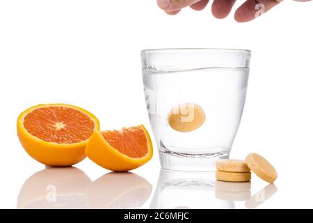 Serie di compresse effervescenti di vitamina C aromatizzate all'arancia cadono e si sciolgono in un bicchiere d'acqua su fondo bianco Foto Stock