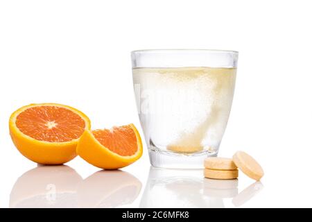 Serie di compresse effervescenti di vitamina C aromatizzate all'arancia cadono e si sciolgono in un bicchiere d'acqua su fondo bianco Foto Stock