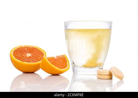 Serie di compresse effervescenti di vitamina C aromatizzate all'arancia cadono e si sciolgono in un bicchiere d'acqua su fondo bianco Foto Stock