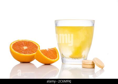 Serie di compresse effervescenti di vitamina C aromatizzate all'arancia cadono e si sciolgono in un bicchiere d'acqua su fondo bianco Foto Stock