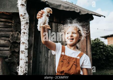 Ritratto di una bella ragazza riccia che tiene in mano un piccolo pollo giallo, godendo la giornata, in una soleggiata giornata estiva. Il concetto di unità o Foto Stock