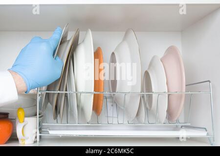 una mano blu con guanti posiziona una piastra pulita sul piano di asciugatura Foto Stock