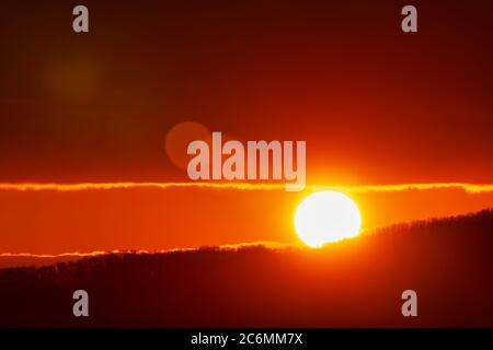Bella alba in montagna, disco solare rosso arancio sorge dalle cime della catena montuosa. Luce naturale del cristallino nel cielo, luce solare che perde. Foto Stock