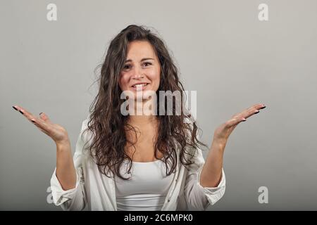 L'umore confuso diffonde le mani con il viso dubbio. In shock. Persone emozioni sincere. Dividono ampiamente le armi in incredulità, delusione e malinteso. Giovane donna attraente, blusa bianca vestita Foto Stock