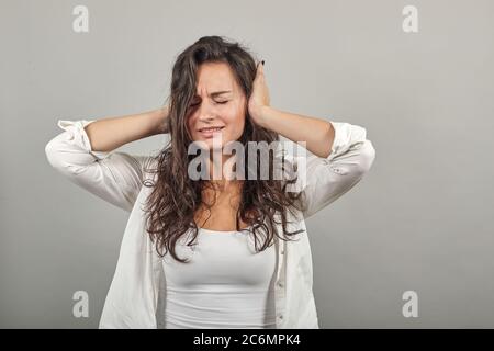 Se si intasano le orecchie con le dita, non si vogliono sentire, mani coperte dell'auricolo, dispiaciuto, blocca il suono, qualcosa è forte. Giovane donna attraente, blusa bianca vestita, con occhi marroni, capelli ricci Foto Stock