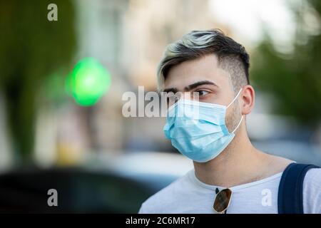 Bel giovane uomo in piedi all'aperto indossando maschera medica per proteggere gli altri dalla diffusione del virus Foto Stock