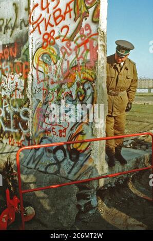 Un Oriente poliziotto tedesco guarda ad un piccolo albero di Natale che ornano il tedesco-occidentale della parte del muro di Berlino. La protezione è in piedi al creato di recente apertura nel muro di Berlino a Potsdamer Platz. Foto Stock