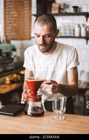 Giovane barista pensante in piedi al banco bar e preparare il caffè mentre si lavora in caffetteria. Foto Stock