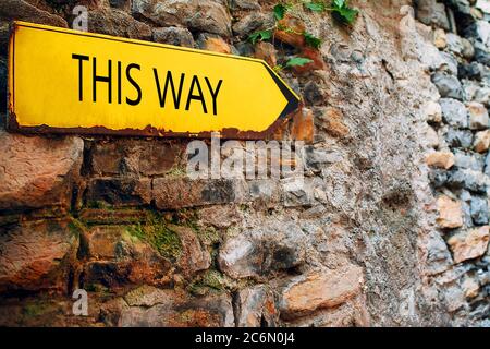 Segno giallo freccia su vecchio muro di pietra mattone. Puntatore di direzione con iscrizione in questo modo. Foto Stock