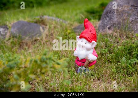 Un tipico goblin da giardino tedesco colorato con un viso sorridente espressione e strumenti in piedi tra pietre e il prato verde nella Foto Stock