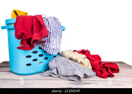 Cesto di bucato pieno di appelli indossati per il lavaggio su tavolo di legno su sfondo bianco Foto Stock