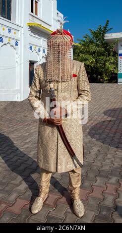 Elegante sposo Sikh in abito tradizionale con pror coprente viso Alla cerimonia di matrimonio e la spada cerimoniale Punjab India Foto Stock