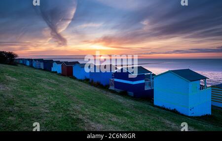 Una scena costiera del Kent; rifugi Whitstable sulla spiaggia sulle pendici di Tankerton al tramonto. Foto Stock