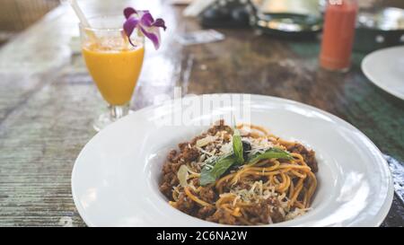 Spaghetti appetitosi sul piatto e succo sul tavolo. Da sopra gustosi tagliatelle fresche su piatto bianco e succo d'arancia in vetro Foto Stock