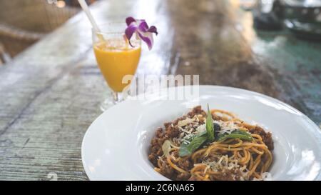 Spaghetti appetitosi sul piatto e succo sul tavolo. Da sopra gustosi tagliatelle fresche su piatto bianco e succo d'arancia in vetro Foto Stock