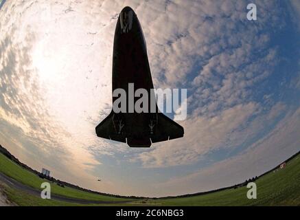 Questa vista insolita del lato inferiore dell'orbiter Atlantis dello Space Shuttle poco prima dell'atterraggio è stata presa da un obiettivo di una telecamera fish-eye proveniente dal servizio di atterraggio dello Shuttle del KSC. L'edificio di assemblaggio del veicolo si trova sullo sfondo a sinistra. L'aereo da addestramento a navetta può essere visto in distanza, al centro. Atlantis sta chiudendo la sua missione STS-84 di nove giorni, che è stato il sesto attracco dello Space Shuttle con la Stazione spaziale russa Mir. Atlantis è stato attraccato con il Mir per cinque giorni. Foto Stock