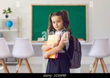 Concetto di ritorno a scuola. La bambina scolastica con i libri nelle sue mani sta in piedi contro la priorità bassa nella classe nella scuola elementare. Foto Stock