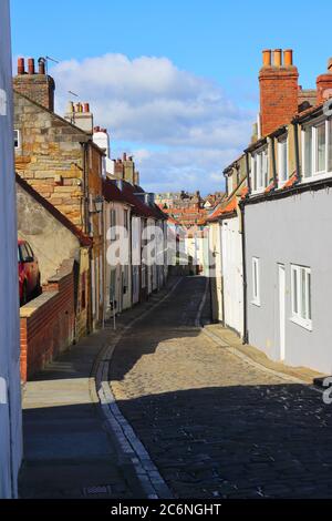 Cobbled Street con cielo blu e case a schiera a Whitby, North Yorkshire, Inghilterra, Regno Unito Foto Stock