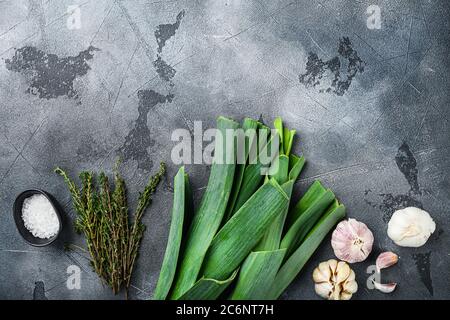 Gambi di porri con erbe ingredienti per cucinare porri brasati, su sfondo grigio testurizzato vista dall'alto con spazio per il testo. Foto Stock